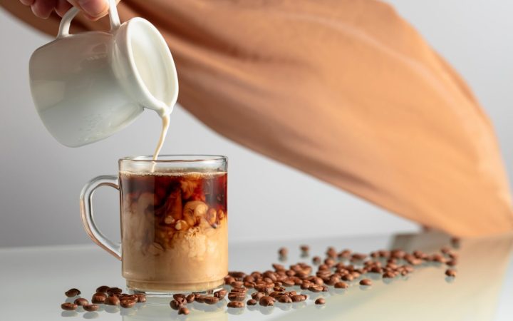 ceașcă transparentă de cafea în care se toarnă lapte