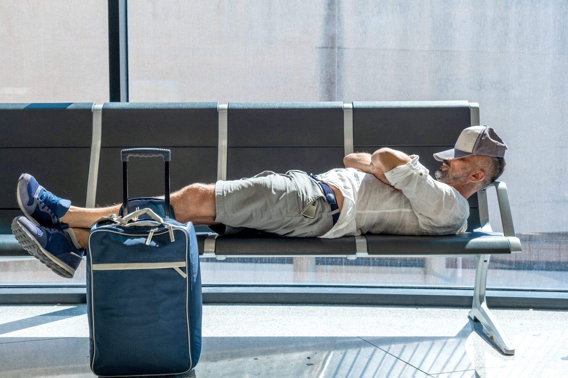 bărbat doarme pe banca din aeroport, cu valiza lângă el