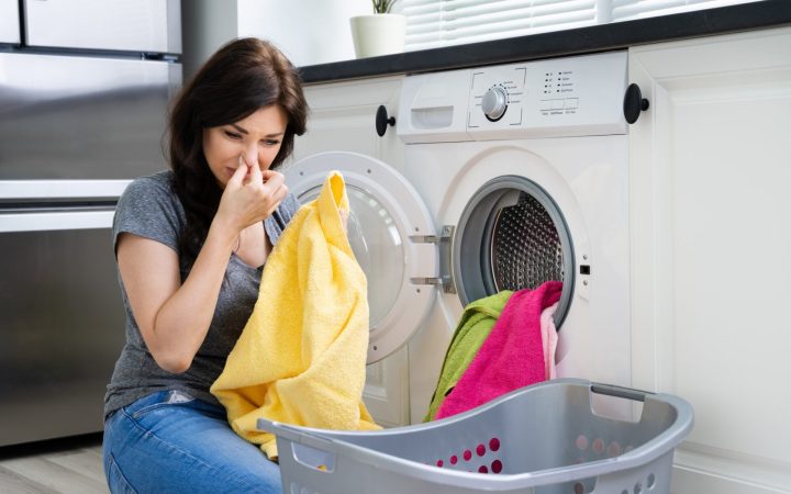 cu ce se curăță mașina de spălat când miroase urât - femeie care scoate rufele urât mirositoare din mașina de spălat